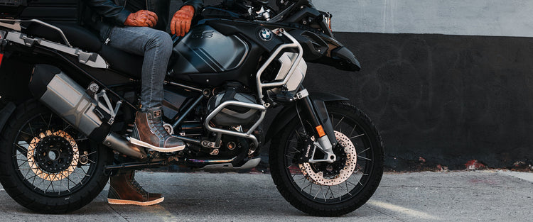 Rider wearing brown Armstrong motorcycle boots and leather gloves on a black BMW adventure motorcycle.