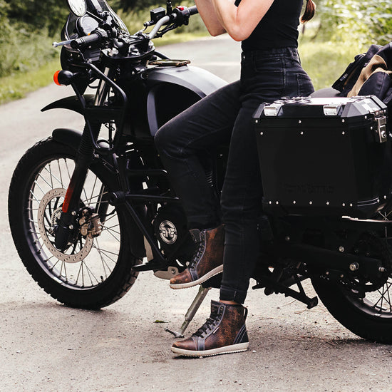 Person sitting on a black Royal Enfield Himalayan motorcycle wearing ventilated motorcycle boots on a gravel road.