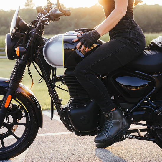 Person sitting on a Royal Enfield motorcycle with hands gripping the tank and wearing black leather motorcycle boots.