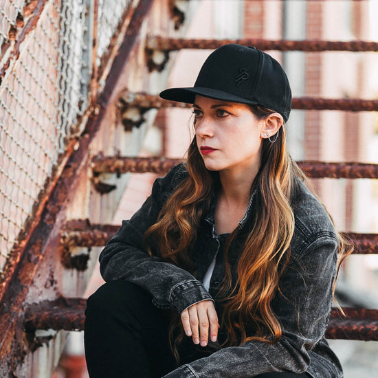 Woman wearing a black cap and dark jacket sitting on a rusted metal staircase.