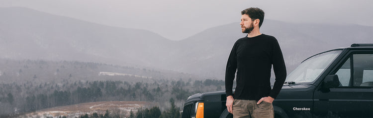 Man standing next to a black Jeep Cherokee SUV in a mountainous landscape