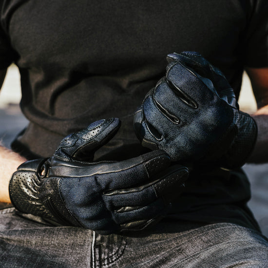 Close-up of black and blue denim gloves held by a person wearing a dark shirt and jeans.