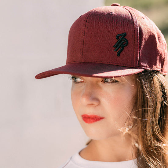 Woman wearing a maroon cap with a logo on a plain background