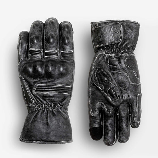 Black leather motorcycle gauntlet gloves shown in flat lay, featuring padded knuckle protection, reinforced fingers, adjustable wrist strap, and extended cuff for riding protection.