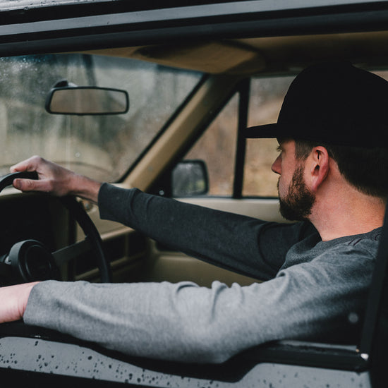 Man driving a vintage Jeep car wearing a black hat and gray Shirt. 