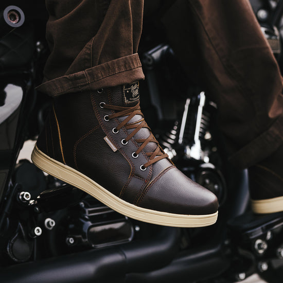 Brown leather boots with beige soles worn by a person sitting on a motorcycle.