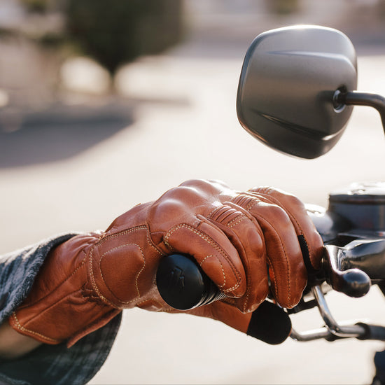 Close-up of a leather gloved hand on a motorcycle handlebar with a blurred street background