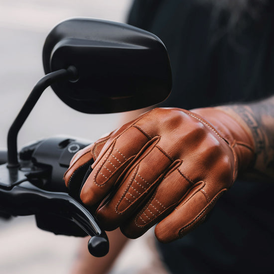 Brown leather glove on a motorcycle handlebar with a blurred background