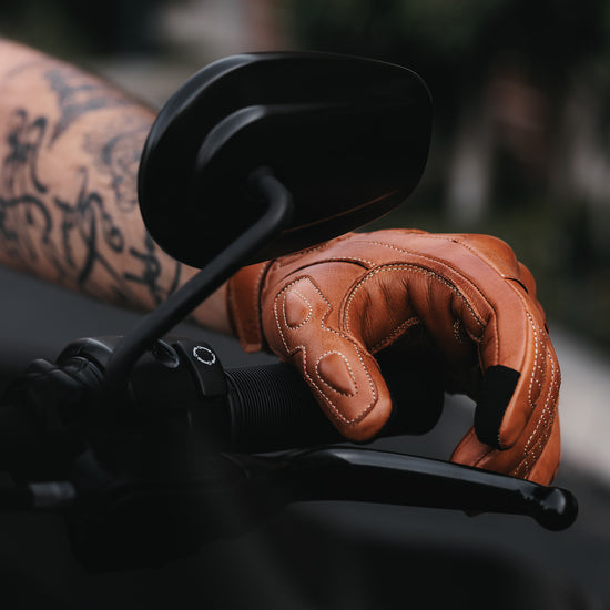 Golden Brown leather glove on a motorcycle handlebar with a blurred background