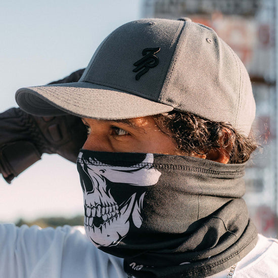 Person wearing a solid gray baseball hat and skull-patterned face mask outdoors