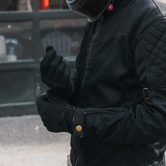 Indie Ridge Powersport motorcycle gloves in black mesh and leather, shown on a rider adjusting the wrist strap while wearing a protective riding jacket.