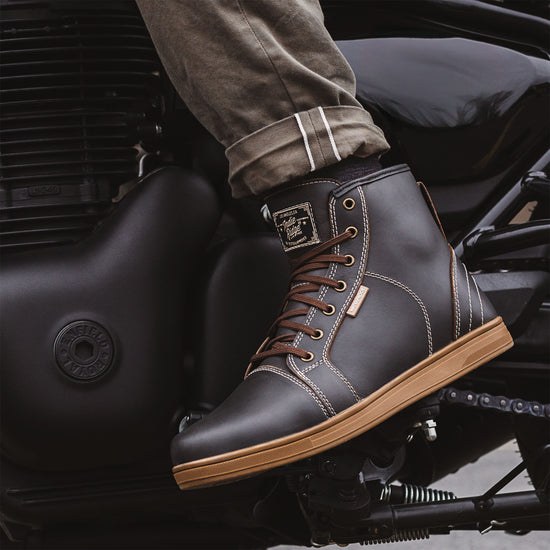 Close-up of Indie Ridge warm brown-gray waterproof leather motorcycle boot on a Royal Enfield while riding, featuring contrast stitching and gum sole.