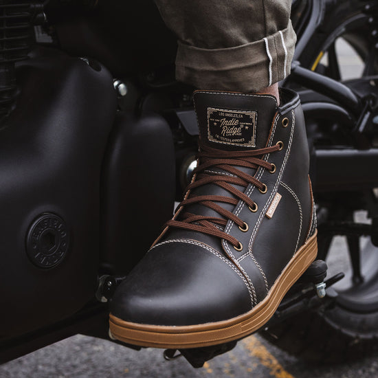 Indie Ridge warm brown-gray motorcycle riding boot on a Royal Enfield foot peg, waterproof full-grain leather construction with reinforced stitching and brown laces.